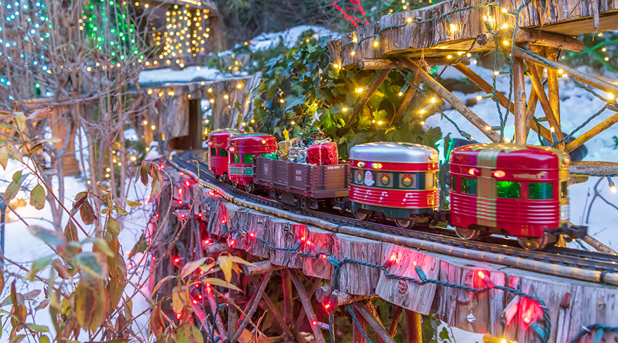 A model train decorated with holiday imagery and colors chugs along the Holiday Garden Railway at Morris Arboretum & Gardens