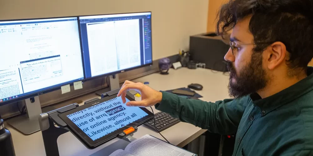 A student uses a screen magnifier to read academic materials in an accessible workspace.