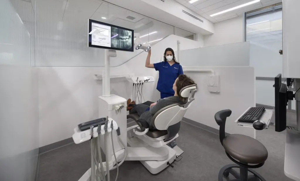 A dental professional in scrubs reviews x-rays with a patient in a modern treatment suite.