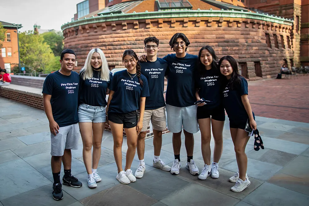 A group of students in matching Pre-First Year Program shirts standing together and smiling on campus.