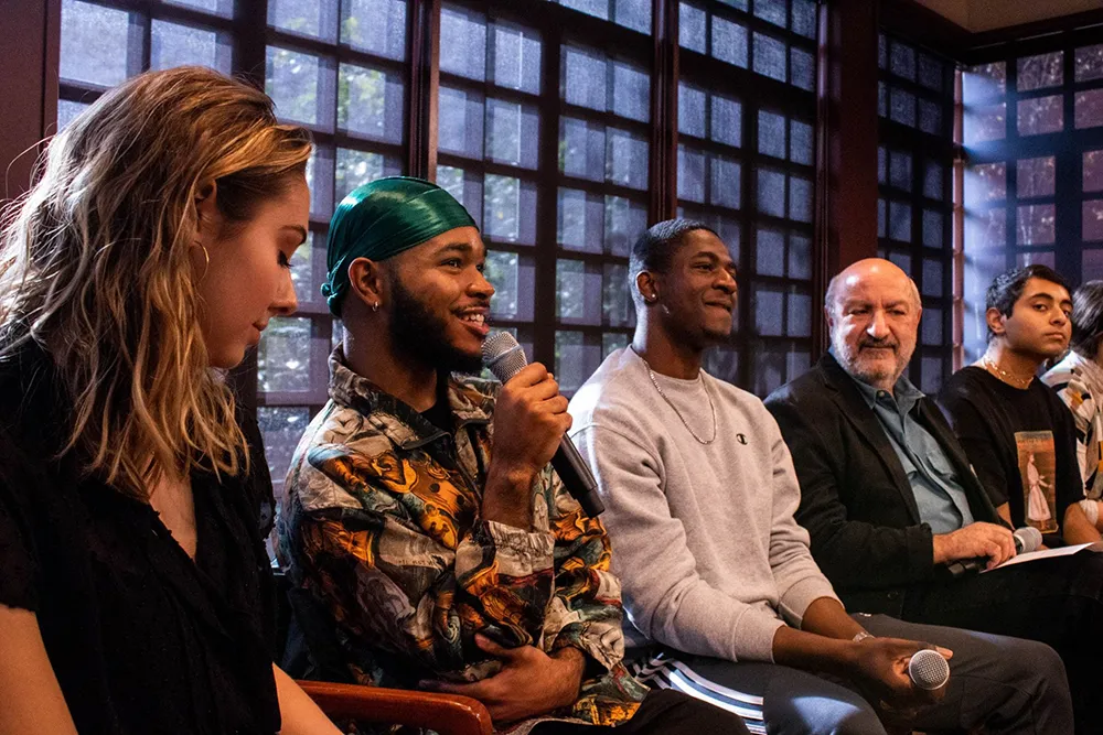 A panel of students and faculty members seated together at Kelly Writers House, with one student speaking into a microphone.