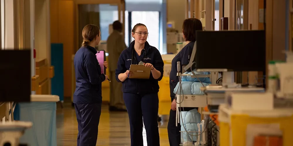 Medical staff stand in discussion near mobile medical carts in a hospital corridor.