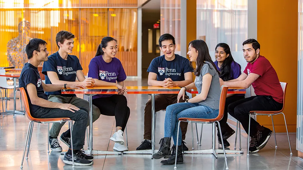 A group of Penn Engineering students seated around a table laughing and talking in a bright common area.