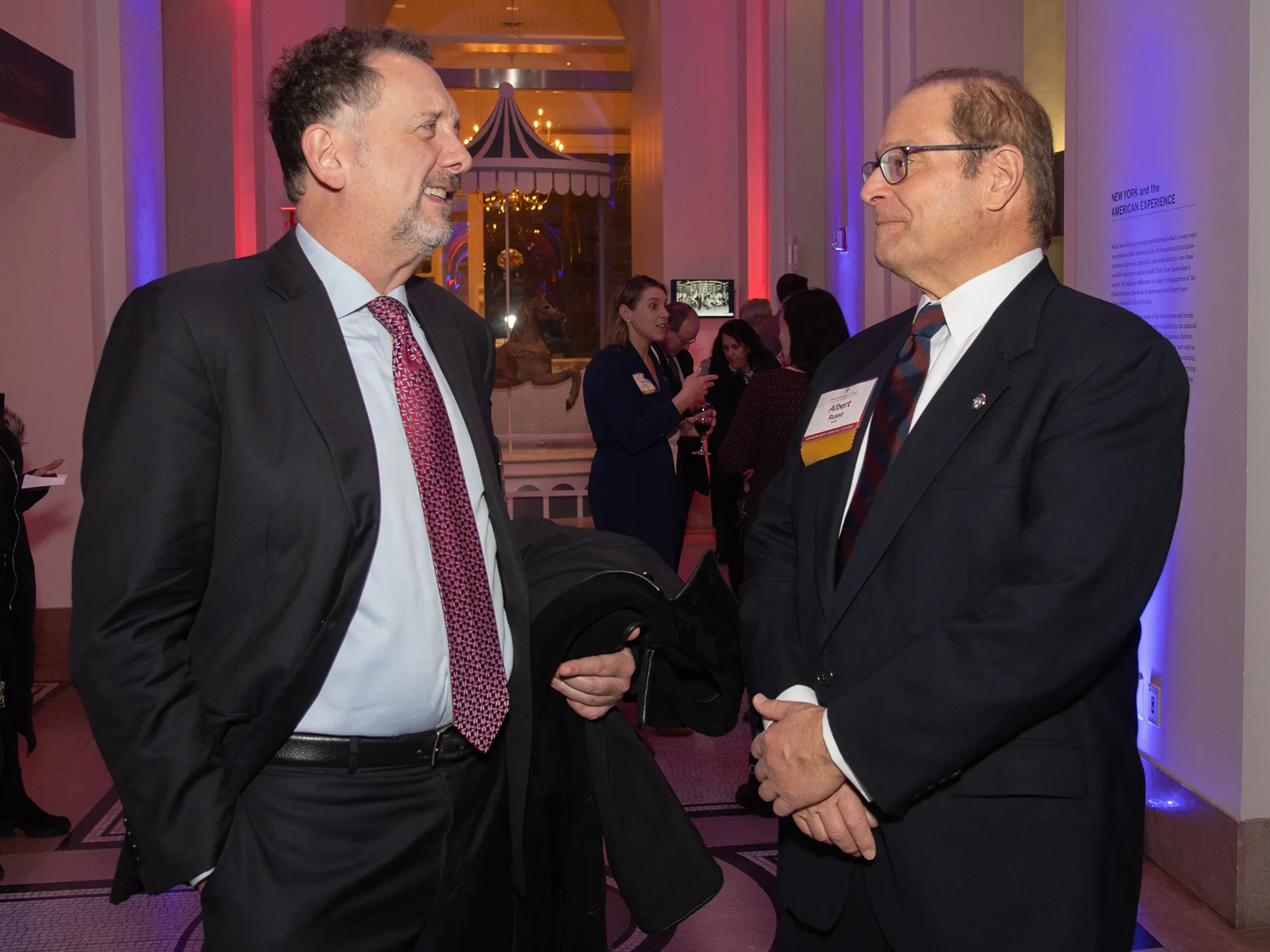 Two Benjamin Franklin Society members engage in conversation at the Spring Reception, standing in an elegantly lit venue.