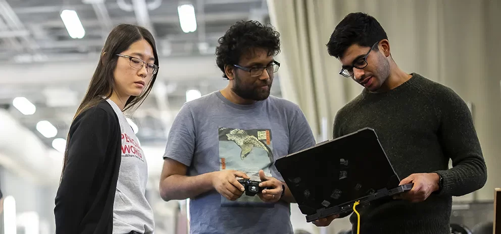 Three students collaborating with a laptop and equipment inside a Penn Engineering lab.