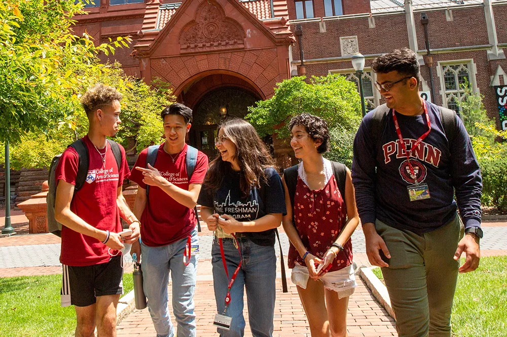 A group of Penn students walking and laughing together on campus in front of Fisher Fine Arts Library.