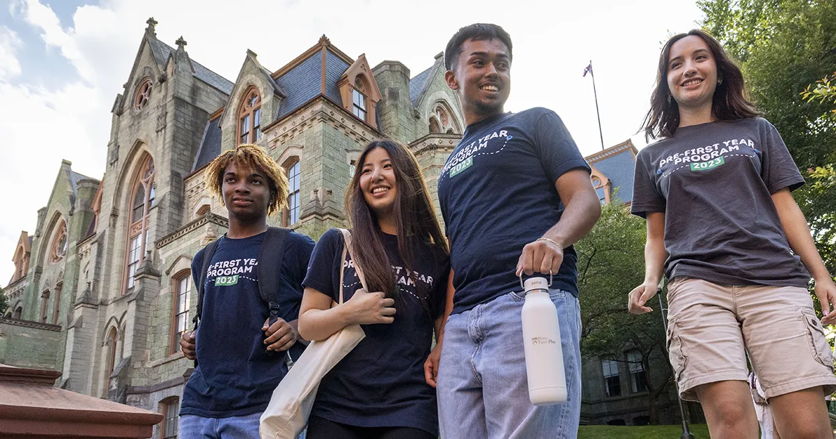A group of five Penn students walks together on the University of Pennsylvania campus in front of College Hall, smiling and chatting.