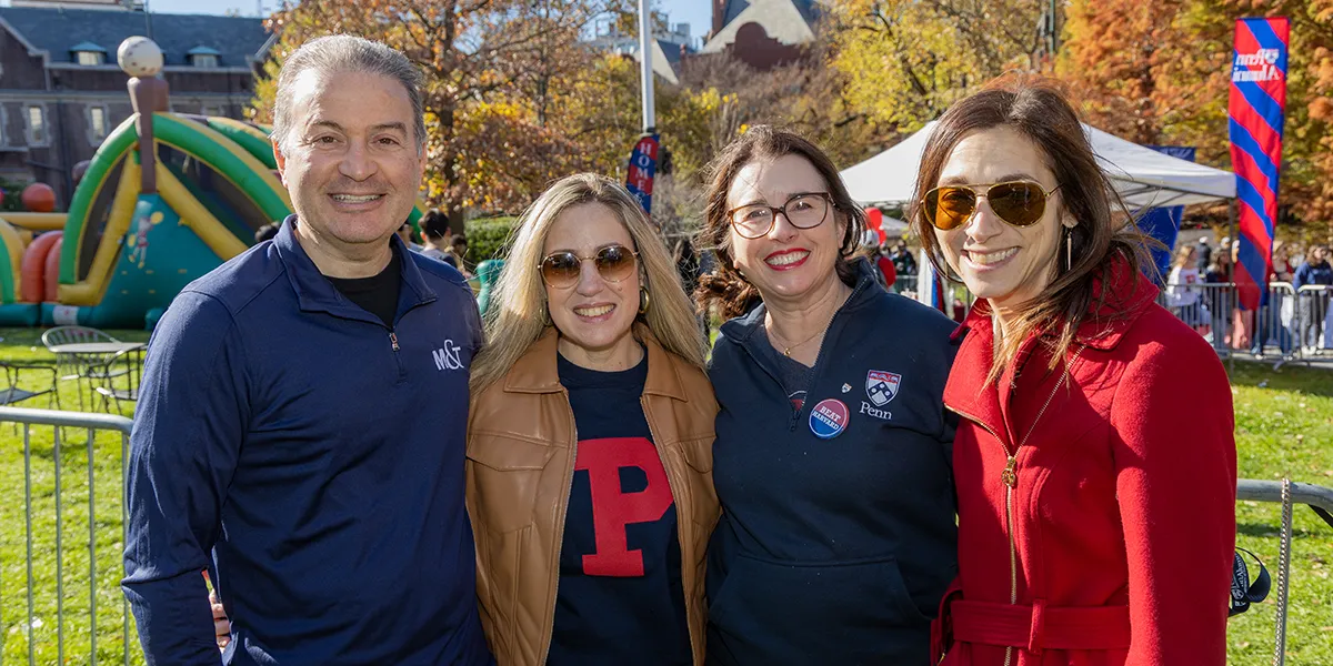 Group of Penn alumni and parents enjoying Homecoming festivities outdoors, posing in front of inflatables and fall foliage on the University of Pennsylvania campus.