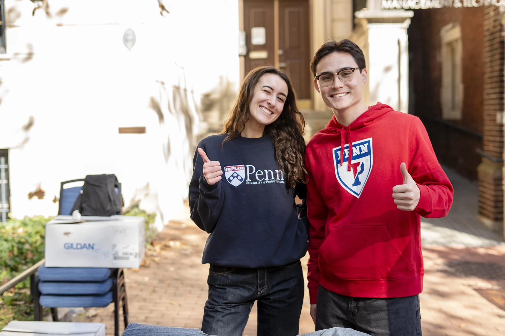 Two Penn Fund staff members smile and give thumbs up while supporting a campus event.