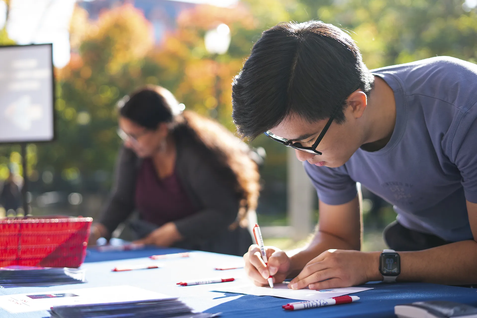 Student writing a thank-you card at a Penn event table with pens and materials laid out.