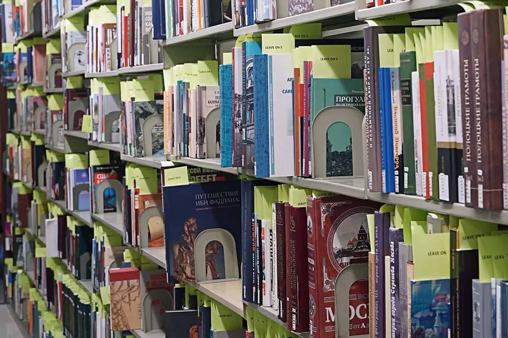 A dense library shelf filled with books from various cultures and regions, many with labels in foreign languages.